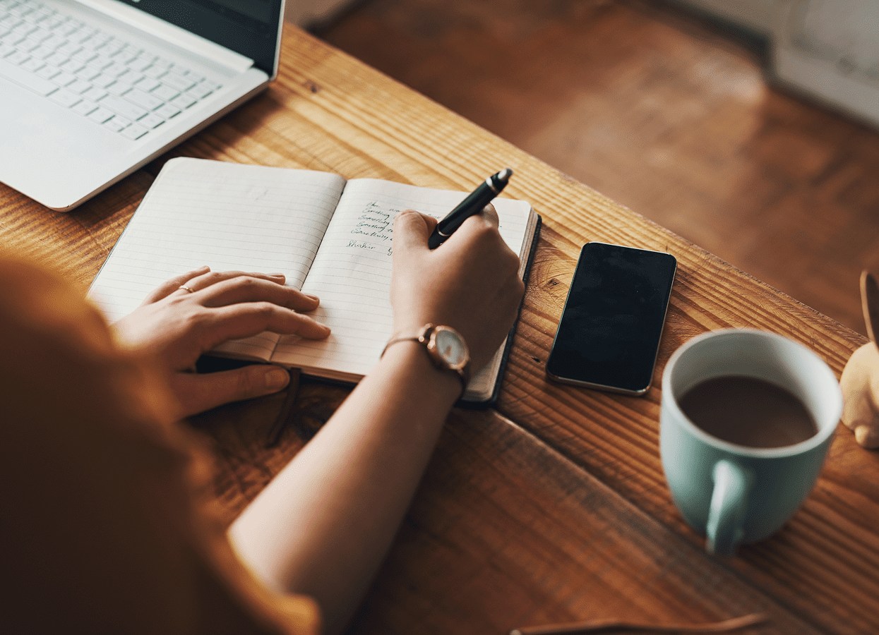 Writing notes with coffee and smartphone nearby.